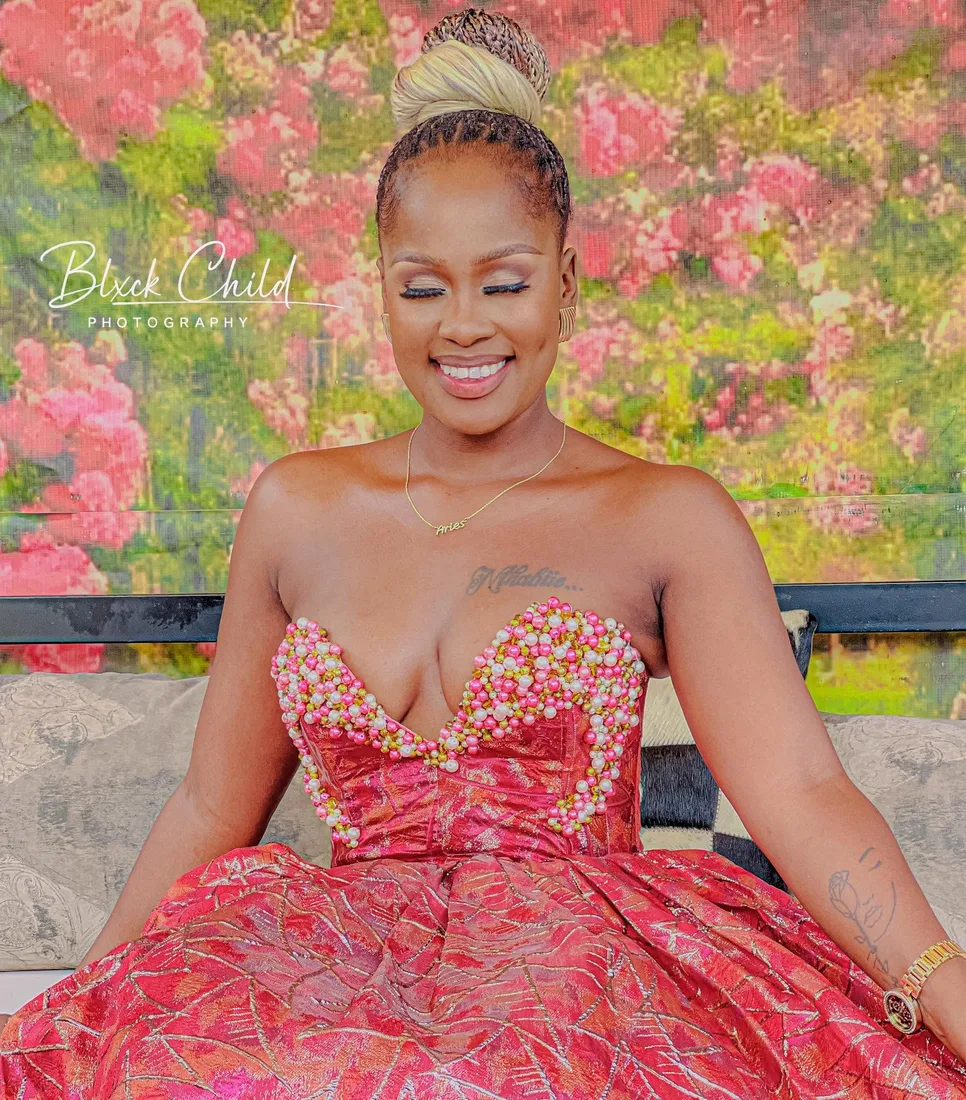 Nthabi smiling in her crimson beaded dress among flowers
